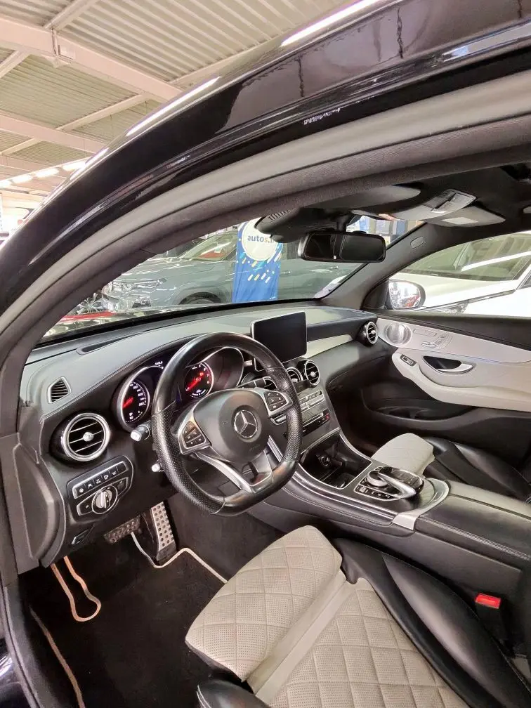 Vue intérieure côté conducteur de la Mercedes GLC 350 Coupé noire, avec sièges cuir beige et tableau de bord moderne.