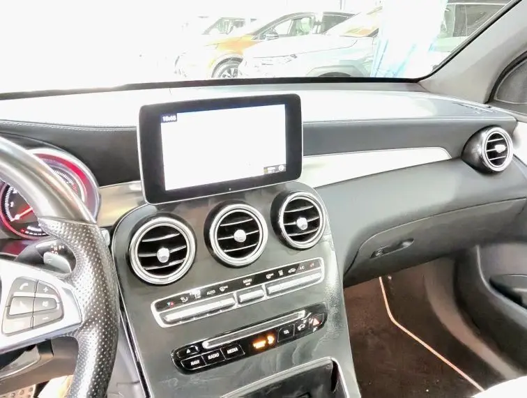 Vue intérieure du tableau de bord et console centrale d'une Mercedes GLC 350 Coupé noire, avec écran tactile et aérateurs ronds.