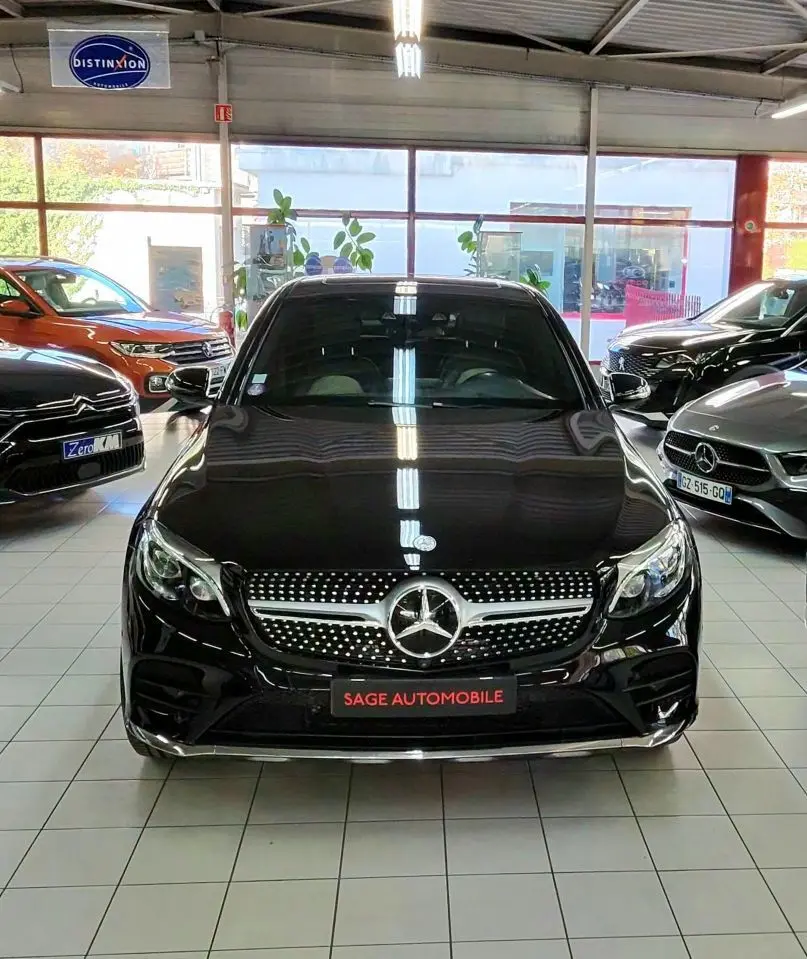 Vue frontale d'un Mercedes GLC 350 Coupé noir brillant en showroom, avec calandre diamantée et logo étoile central.
