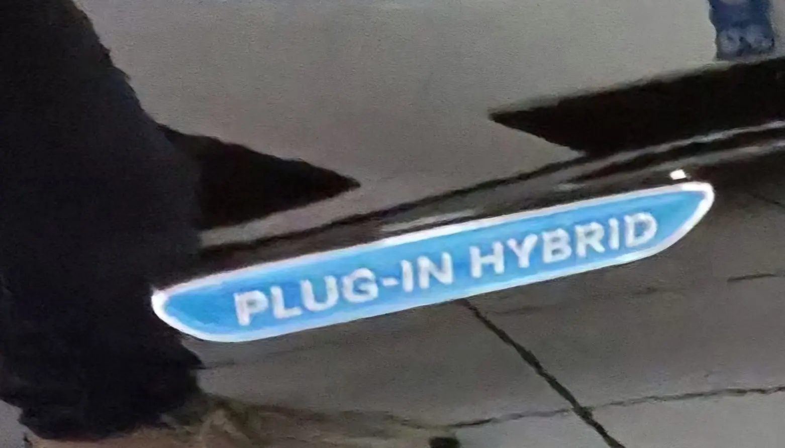 Gros plan sur l’inscription bleue "PLUG-IN HYBRID" sur la carrosserie noire d’une Mercedes GLC Coupé.
