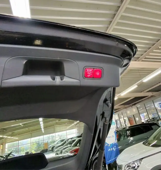Détail intérieur du hayon ouvert d’un Mercedes GLC Coupé noir, montrant la poignée et le bouton stop électrique rouge.