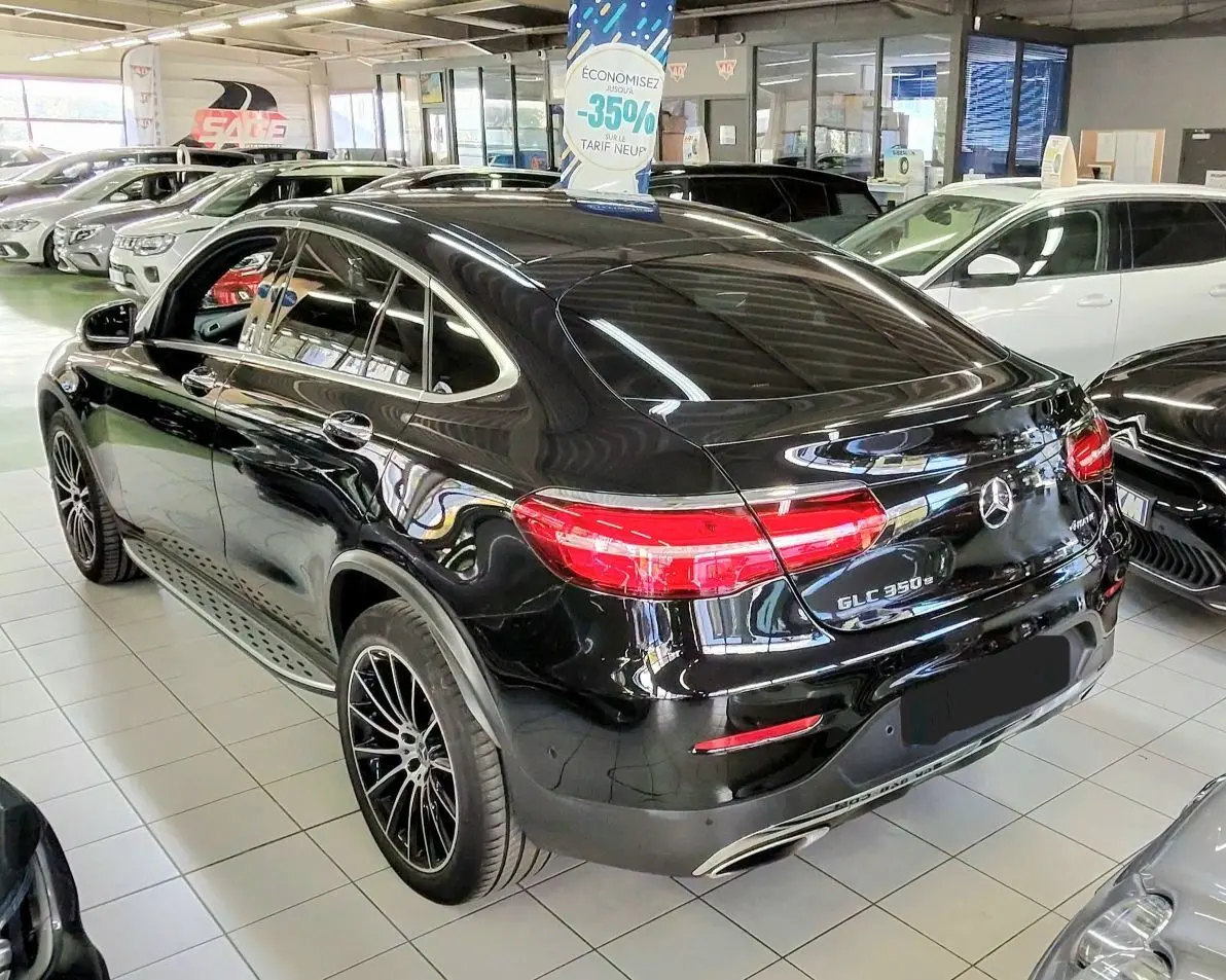 Vue 3/4 arrière droite d’un Mercedes GLC 350 Coupé noir brillant en showroom, avec feux arrière allumés et jantes noires.