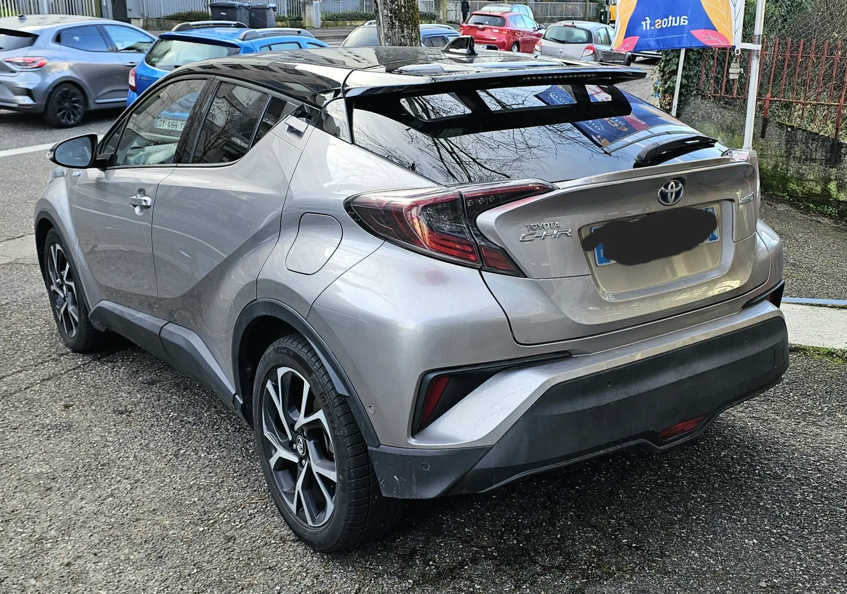 Vue 3/4 arrière droite d’un Toyota C-HR hybride gris 2018 avec toit noir et feux arrière distinctifs.