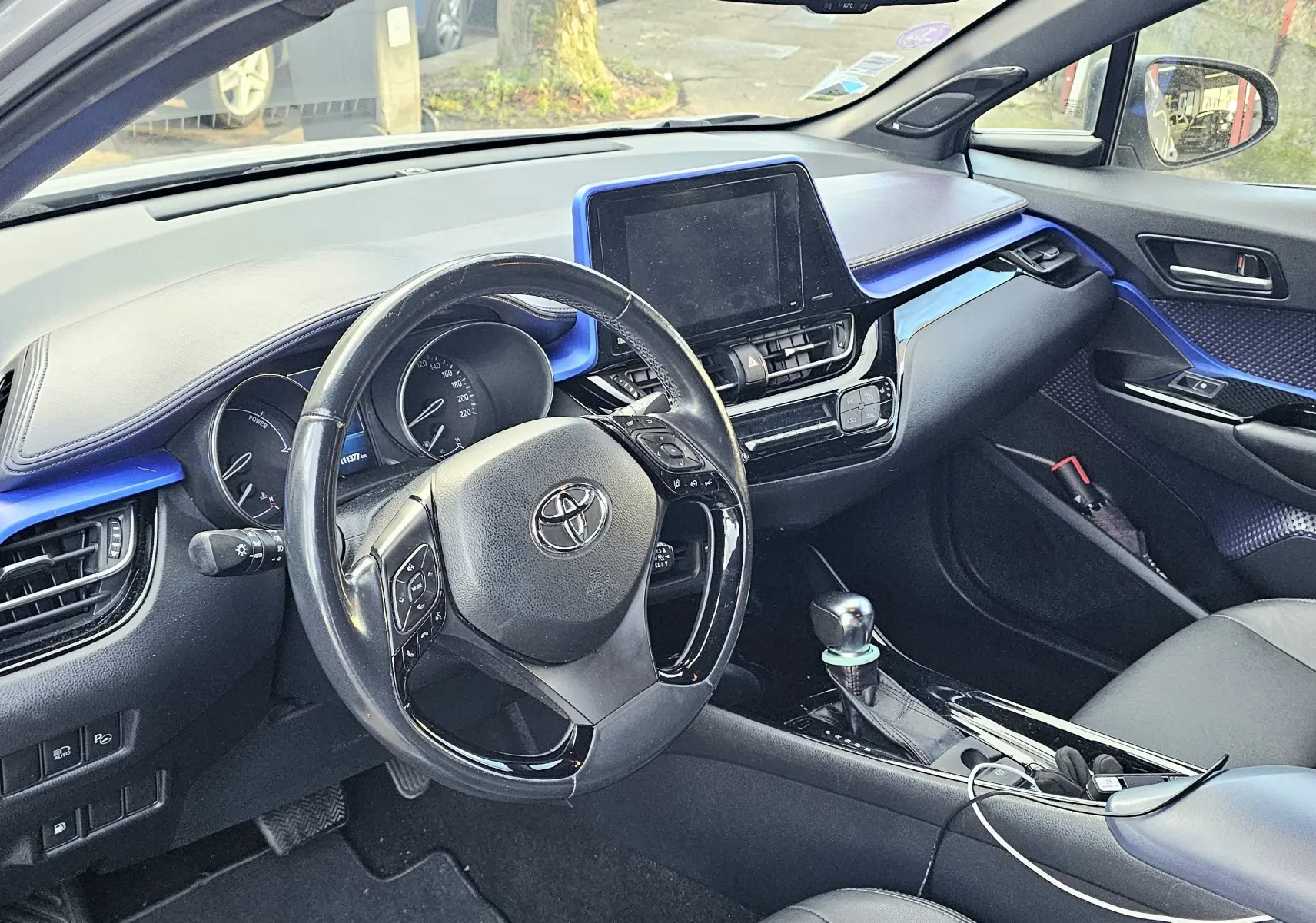 Vue intérieure côté conducteur du Toyota C-HR hybride gris 2018, avec tableau de bord et inserts bleus distinctifs.