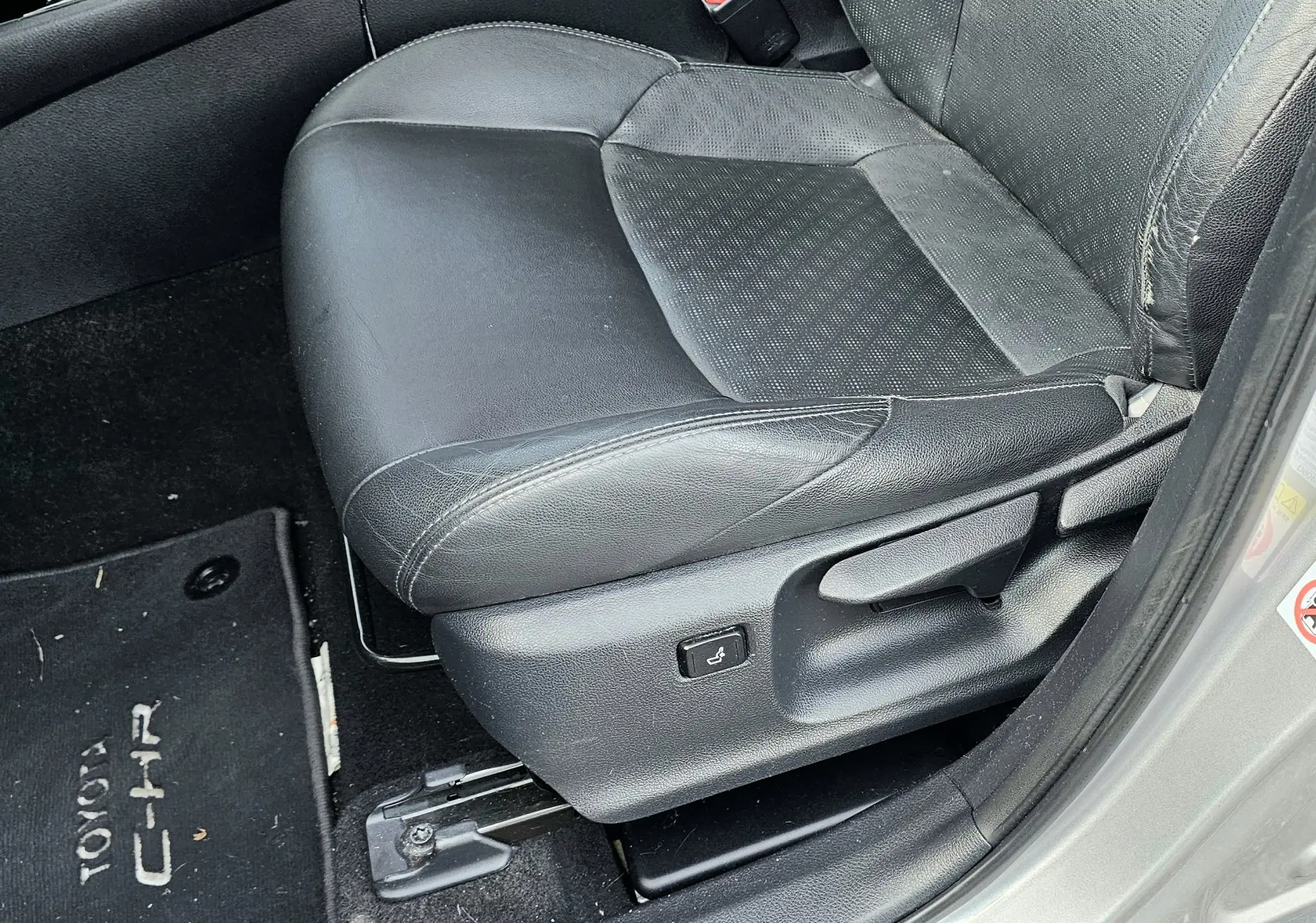 Gros plan sur le siège conducteur en cuir noir du Toyota C-HR hybride gris, avec réglage électrique visible côté gauche.