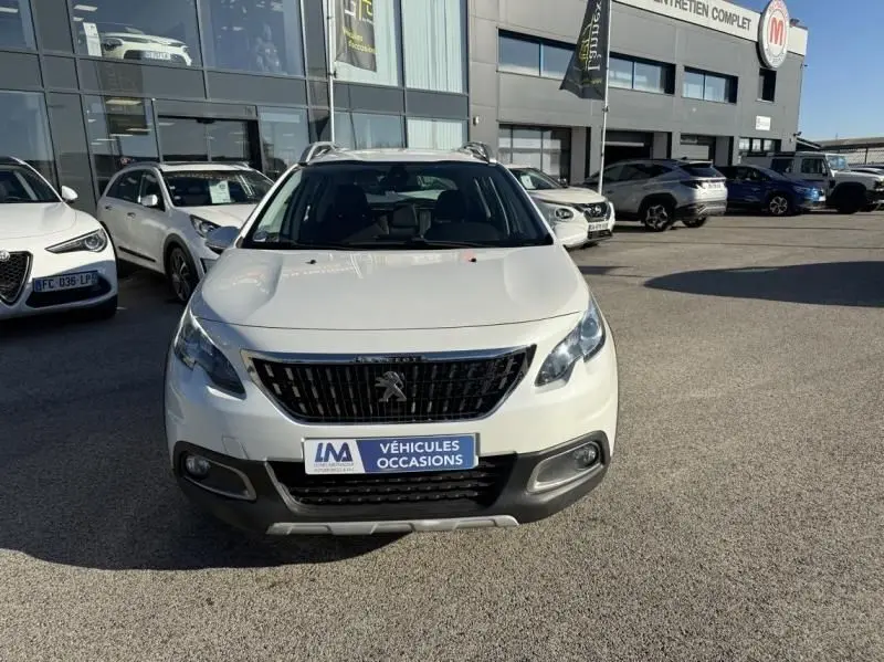 Vue avant d'un Peugeot 2008 blanc de 2018, version 1.2 PureTech 110 Allure, avec calandre noire et plaque "Véhicules Occasions".
