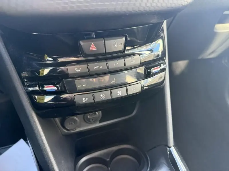 Vue rapprochée de la console centrale noire du Peugeot 2008 blanc, montrant les commandes de climatisation et les boutons de sécurité.