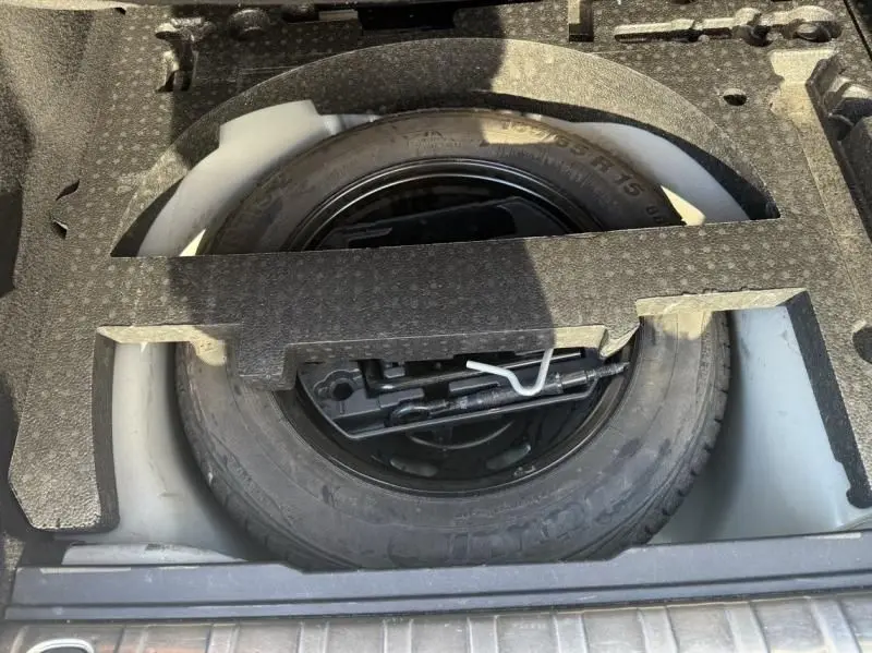 Roue de secours noire dans le coffre d'une Peugeot 2008 blanche, vue plongeante sur l'espace de rangement.