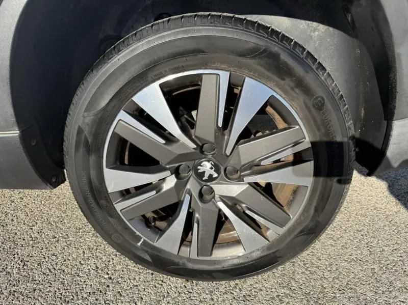 Gros plan sur la roue avant droite d'un Peugeot 2008 blanc, mettant en valeur la jante alliage au design moderne.