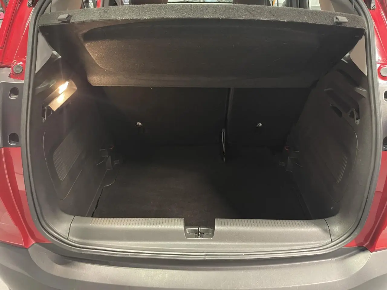 Coffre ouvert vu de l'arrière d'un Opel Crossland rouge clair, montrant l'espace de chargement vide et l'éclairage intérieur.