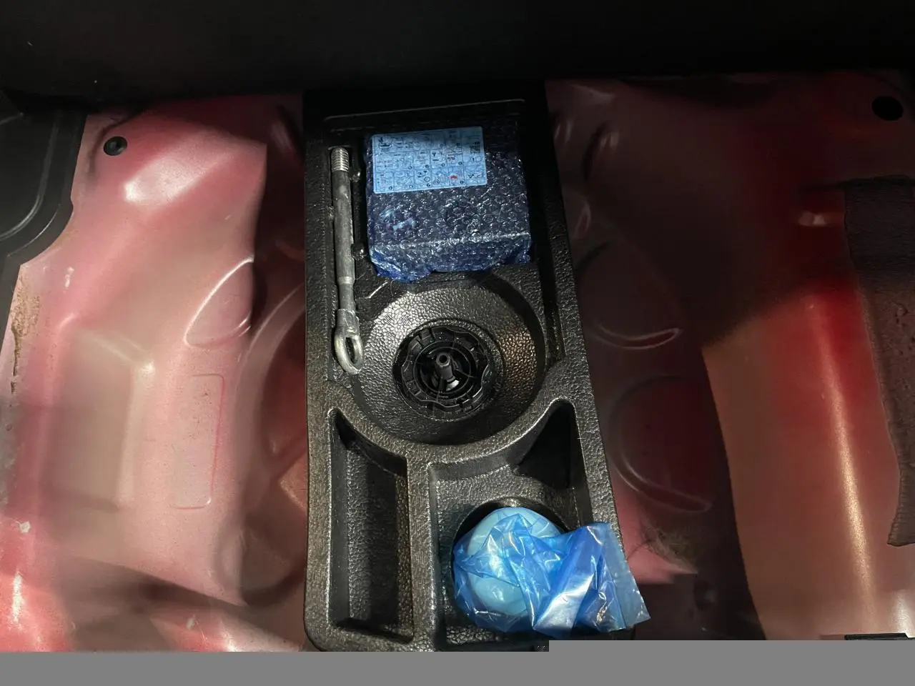 Vue rapprochée du coffre d’une Opel Crossland rouge clair montrant le rangement pour kit anti-crevaison.