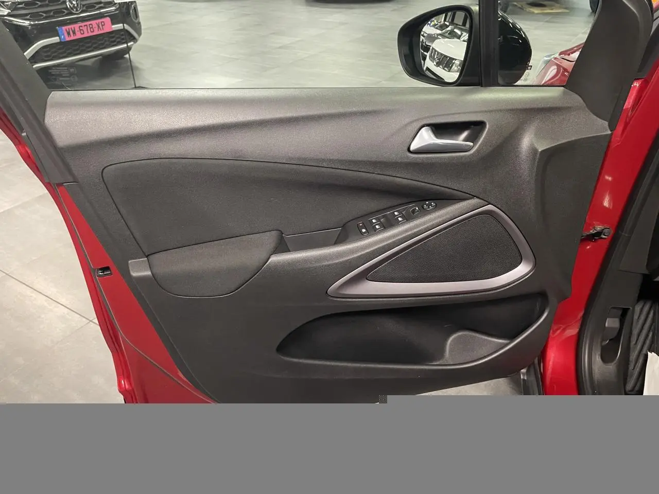 Vue intérieure de la porte avant gauche rouge clair de l’Opel Crossland avec commandes électriques et haut-parleur intégré.