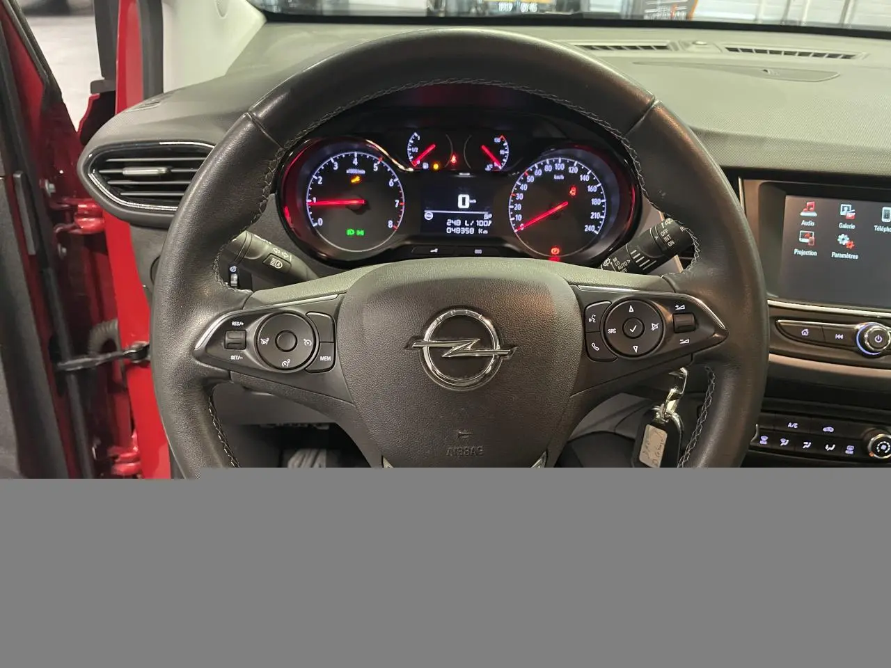 Vue intérieure centrée sur le volant en cuir multifonction de l’Opel Crossland rouge clair avec tableau de bord et écran tactile.