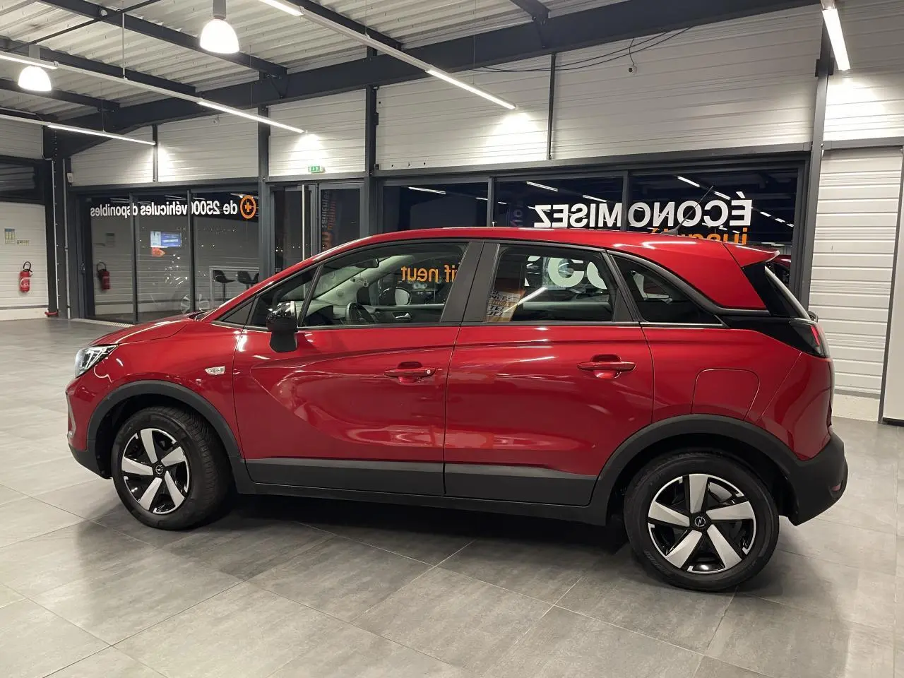 Vue latérale droite d’un Opel Crossland rouge clair 2022 avec jantes bicolores et toit assorti à la carrosserie.