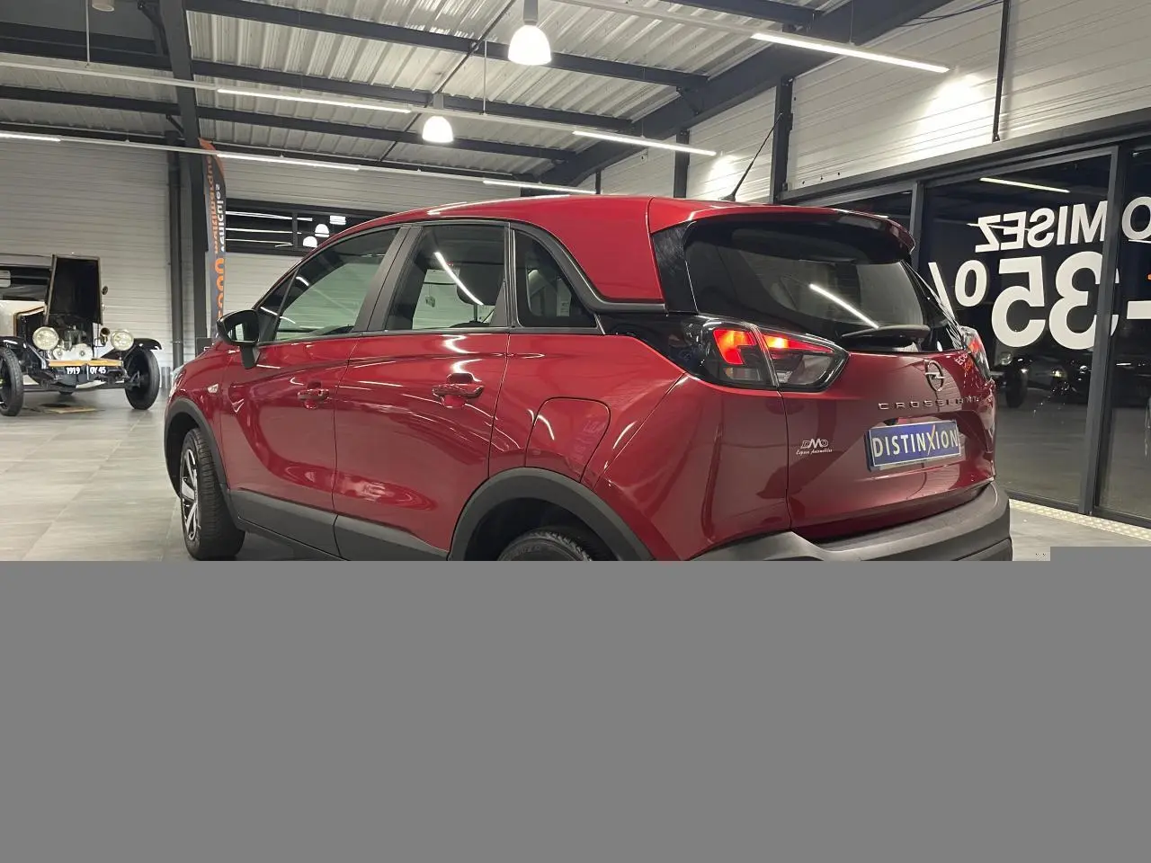 Vue 3/4 arrière droite d’un Opel Crossland rouge clair avec toit noir et jantes bicolores en intérieur showroom.
