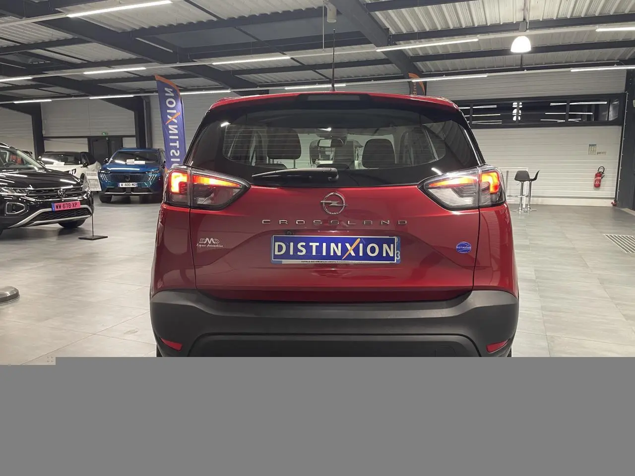 Vue arrière d'un Opel Crossland rouge clair 2022 avec feux allumés et logo Distinxion en concession.