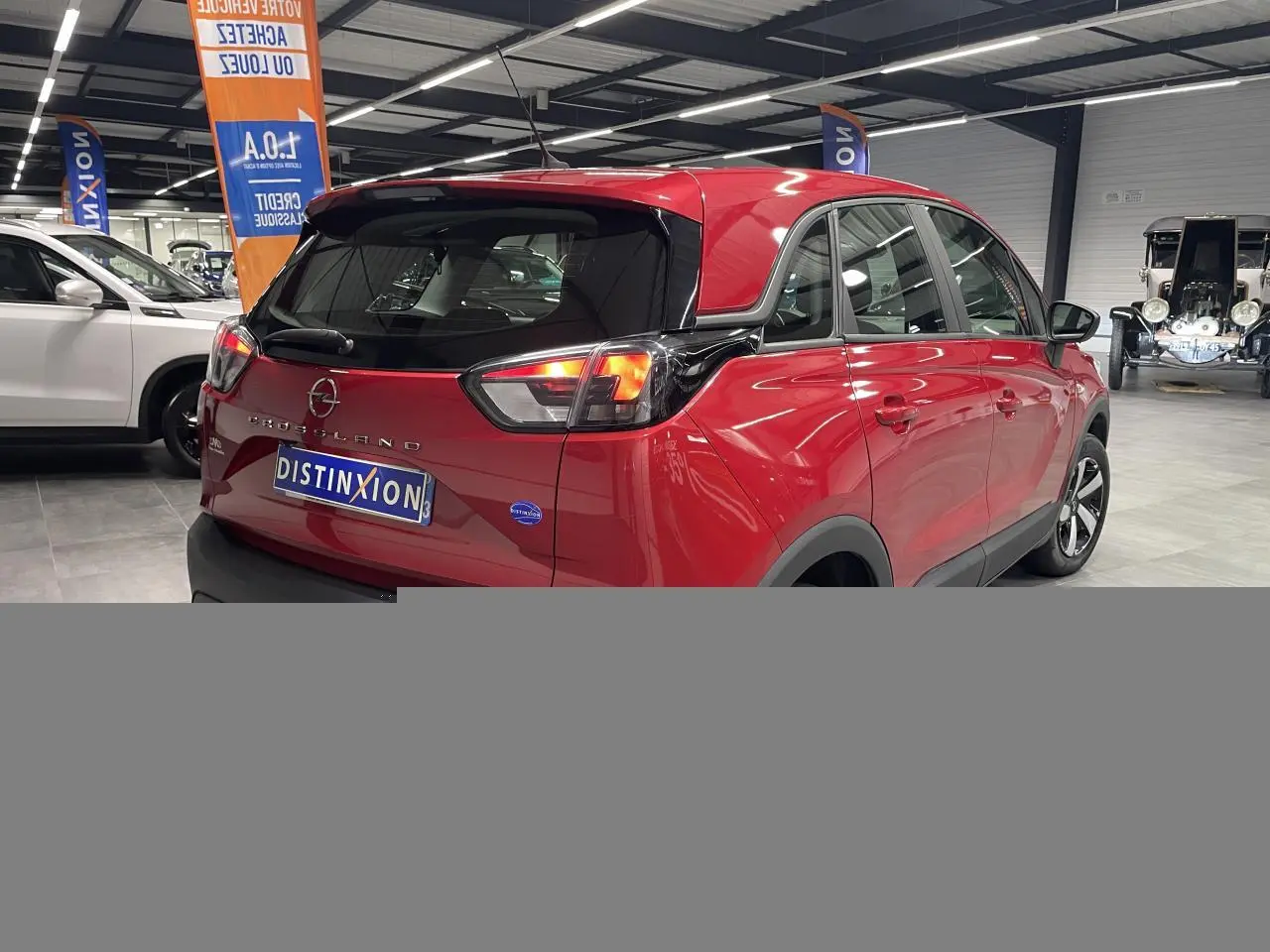Vue 3/4 arrière droite d’un Opel Crossland rouge clair avec toit noir et jantes bicolores en showroom.