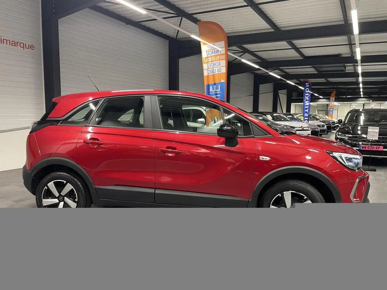 Opel Crossland rouge clair vue de profil droit en intérieur, avec coques de rétroviseurs noires et jantes bicolores.