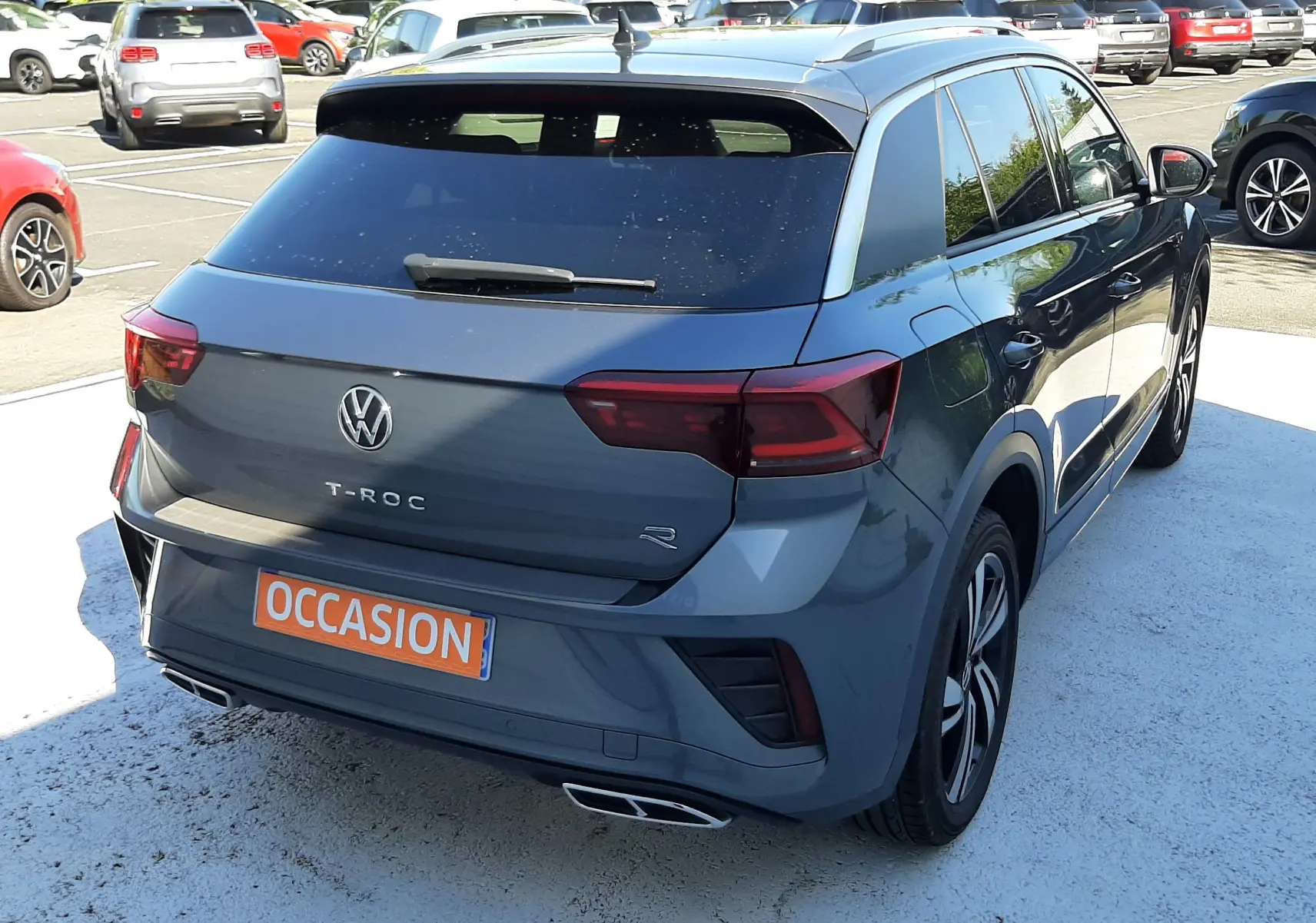 Volkswagen T-Roc gris Indium vu en 3/4 arrière droit, avec feux LED et double sortie d’échappement chromée.