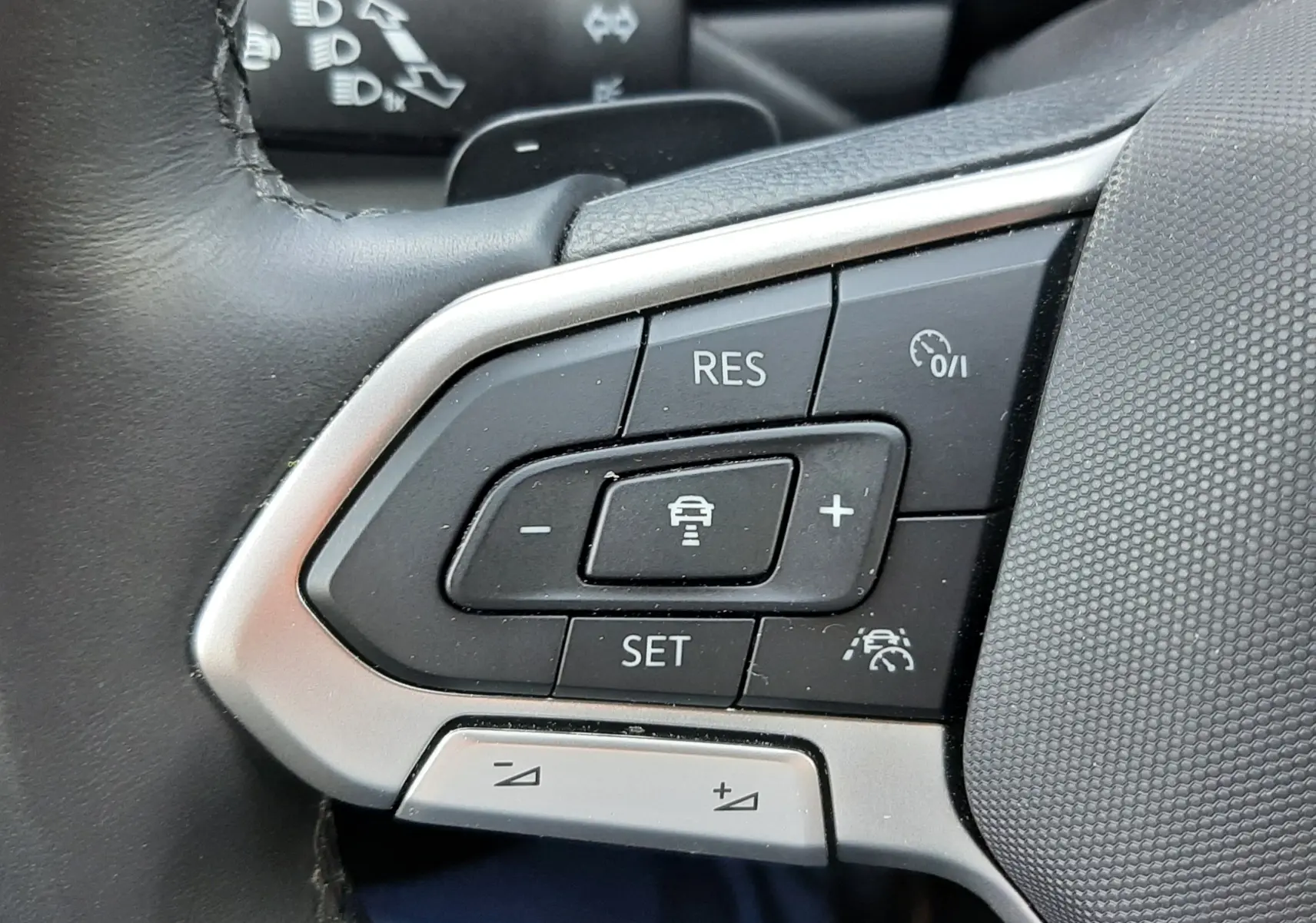 Gros plan sur les commandes de régulateur de vitesse au volant noir du Volkswagen T-Roc gris Indium 2024.