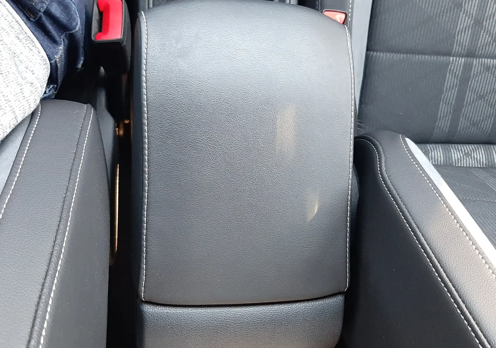 Vue rapprochée de l'accoudoir central en cuir noir avec surpiqûres blanches dans l'habitacle du Volkswagen T-Roc 2024.