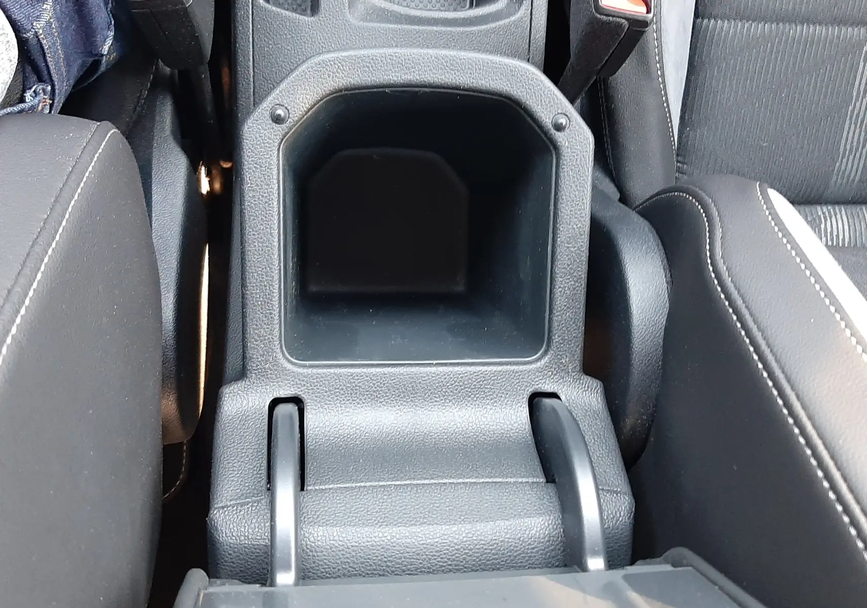 Vue plongeante sur la console centrale noire du Volkswagen T-Roc 2024, avec accoudoirs et ceintures de sécurité visibles.