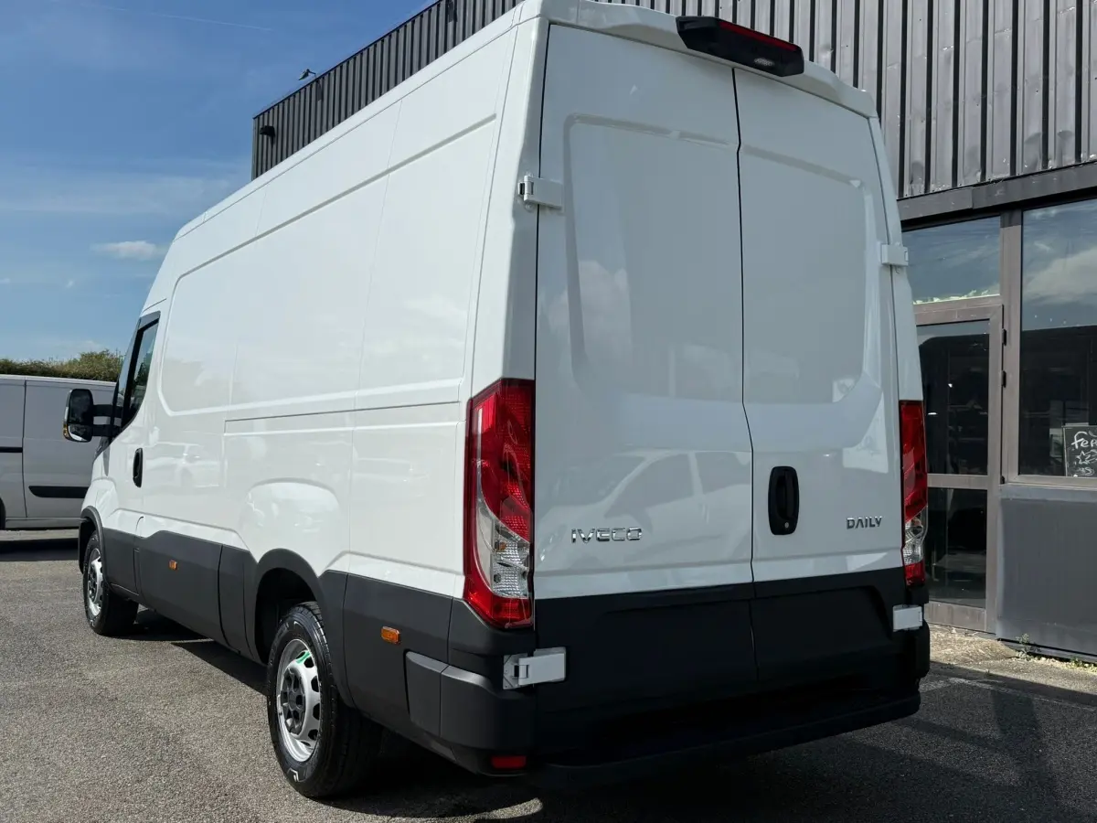 Vue 3/4 arrière droite d’un utilitaire Iveco Daily blanc 2026 avec portes arrière battantes et feux rouges verticaux.