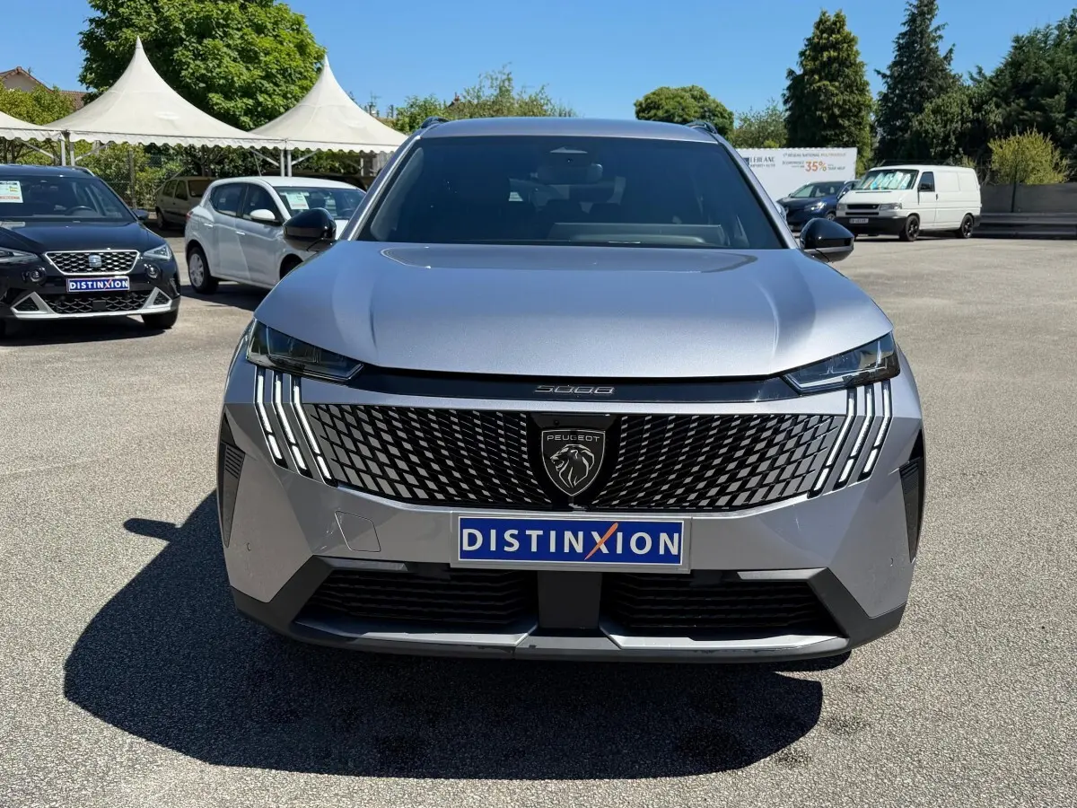 Vue de face d’un Peugeot 5008 gris clair 2025 avec calandre noire distinctive et feux LED verticaux.
