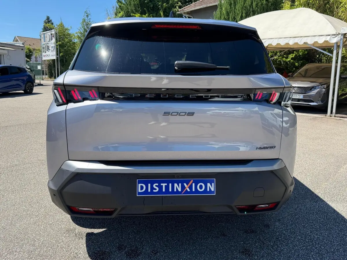 Vue arrière d’un Peugeot 5008 gris clair hybride, avec feux LED distinctifs et logo Peugeot noir brillant.