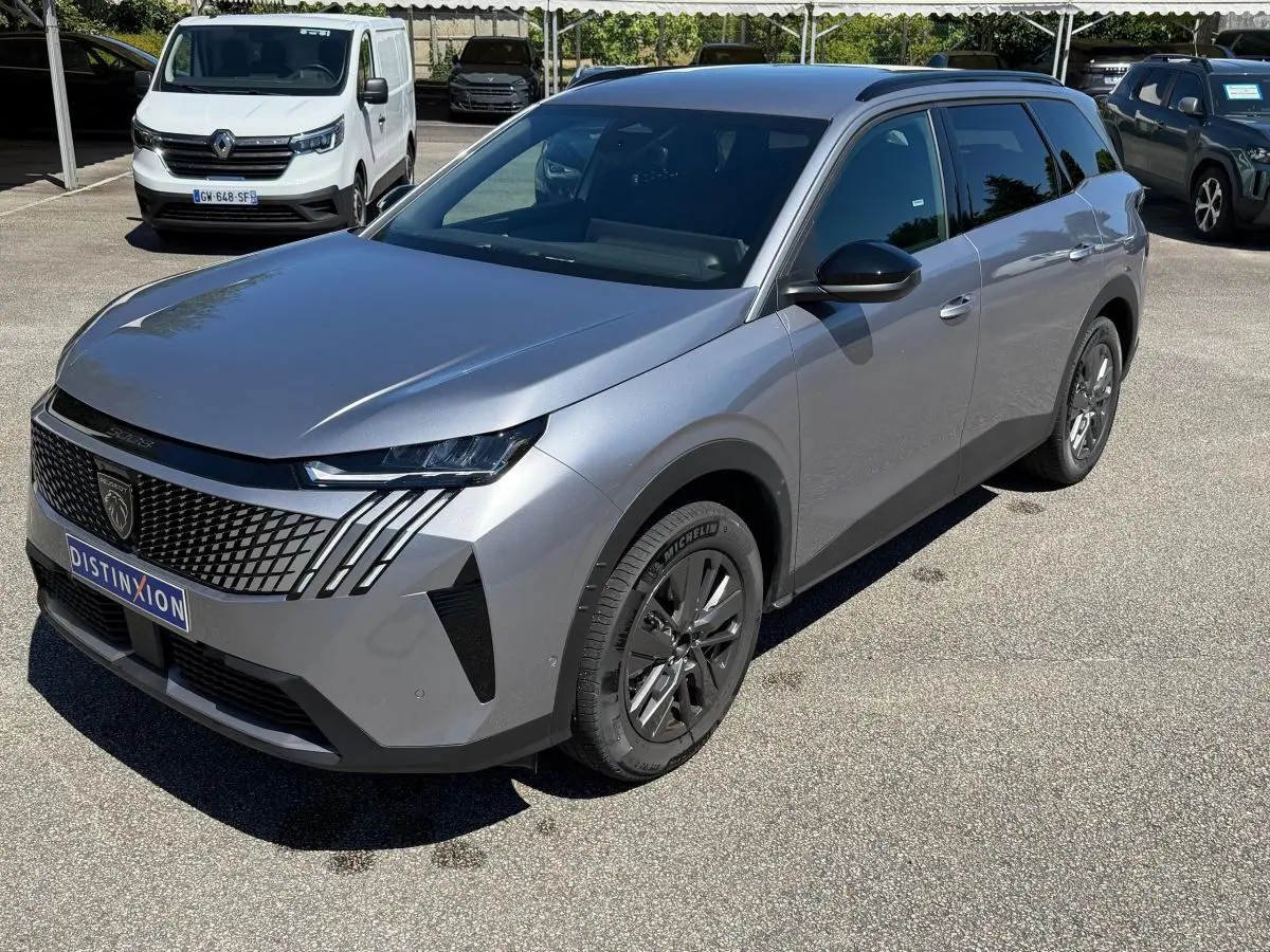 Vue 3/4 avant droit d’un Peugeot 5008 gris clair avec calandre noire et jantes foncées sur parking extérieur.