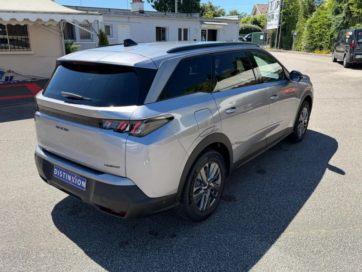 Vue 3/4 arrière droit d’un Peugeot 5008 gris clair hybride avec feux arrière LED et vitres teintées.