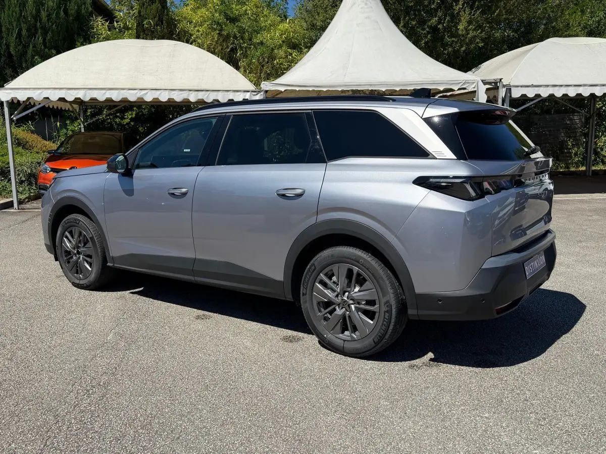 Peugeot 5008 gris clair vue 3/4 arrière droit, SUV hybride avec vitres arrière teintées et jantes foncées.