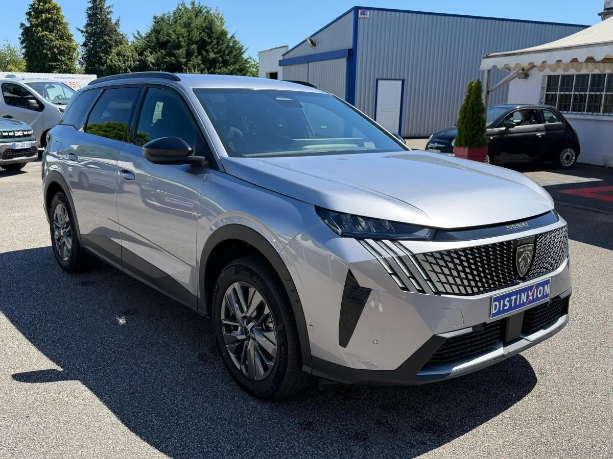 Peugeot 5008 gris clair vue 3/4 avant droit, avec calandre distinctive et phares LED en journée.