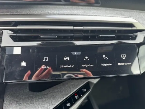 Vue rapprochée de l'écran tactile central noir du tableau de bord du Peugeot 5008 gris clair, affichant les icônes multimédia et navigation.