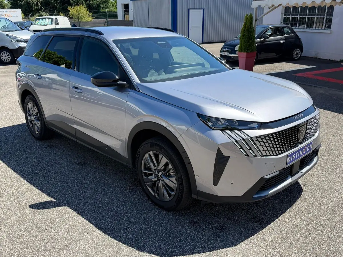Peugeot 5008 gris clair vue 3/4 avant, avec calandre distinctive et feux LED effilés, stationné en extérieur.