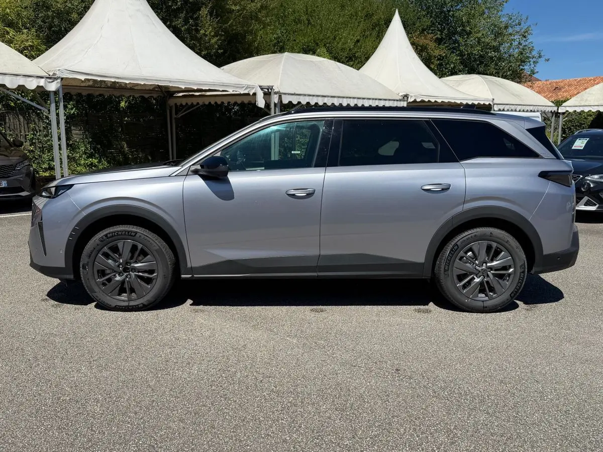 Vue de profil côté gauche d’un Peugeot 5008 gris clair 2025 avec jantes foncées et toit panoramique noir.