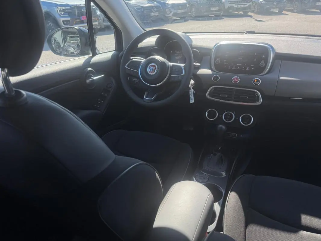 Vue intérieure avant du tableau de bord et volant du Fiat 500X MY23 avec écran tactile et commandes au volant.