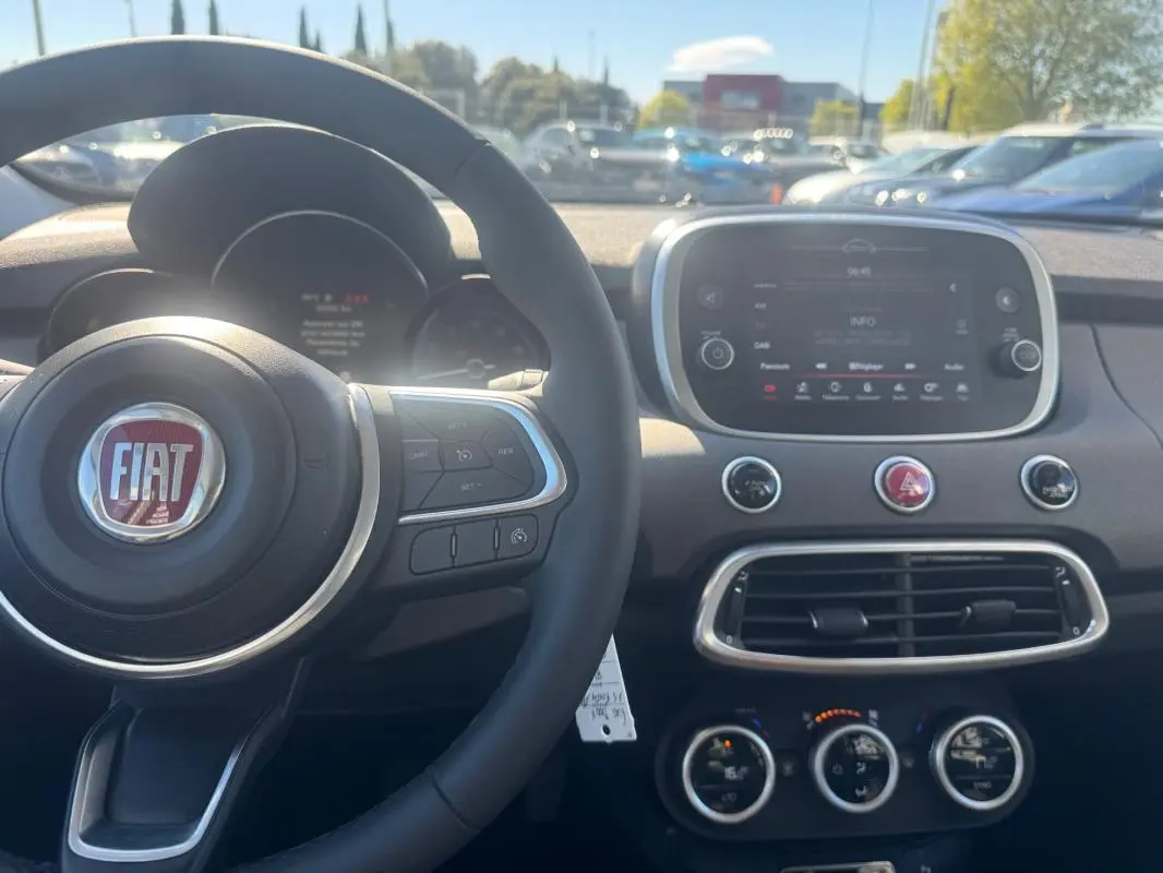Vue intérieure du tableau de bord de la Fiat 500X bleu MY23, avec volant, écran tactile et commandes de climatisation visibles.