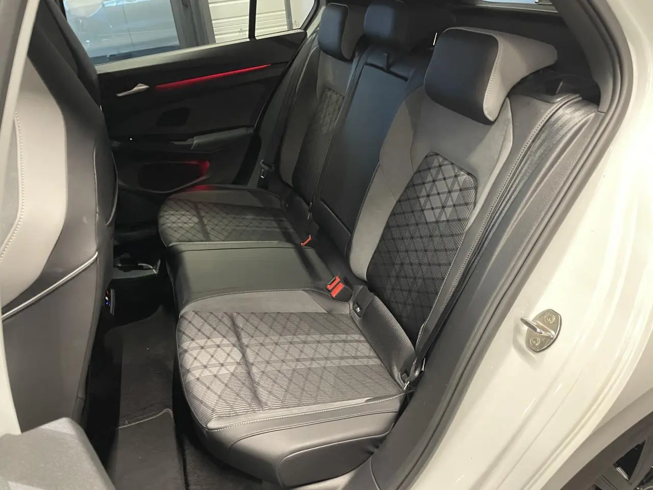 Vue intérieure côté droit sur la banquette arrière en cuir noir et tissu gris avec surpiqûres en losange d'une Volkswagen Golf blanche.