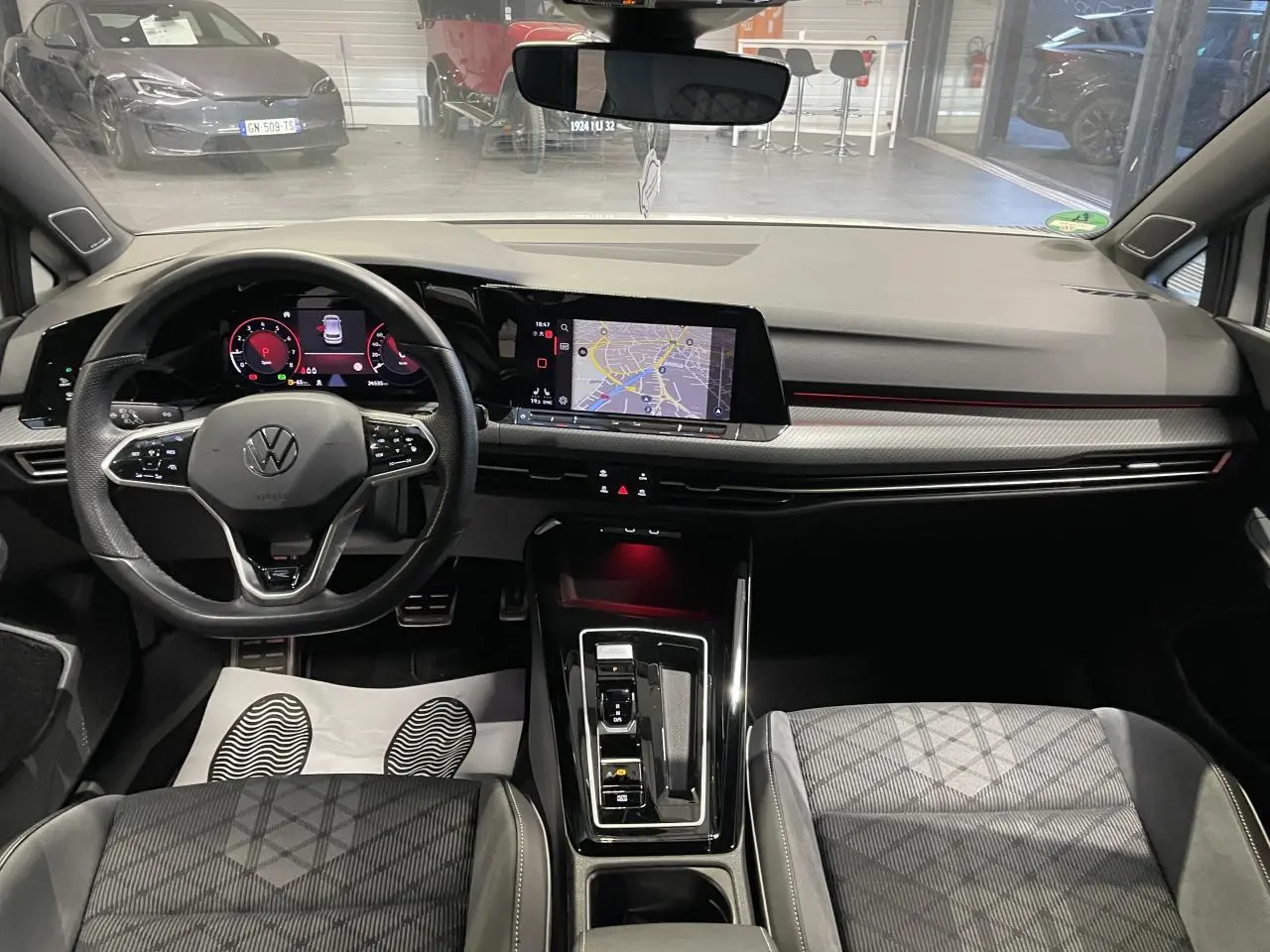 Vue intérieure avant de la Volkswagen Golf VIII R-Line blanche, tableau de bord avec écran tactile et volant multifonctions cuir.