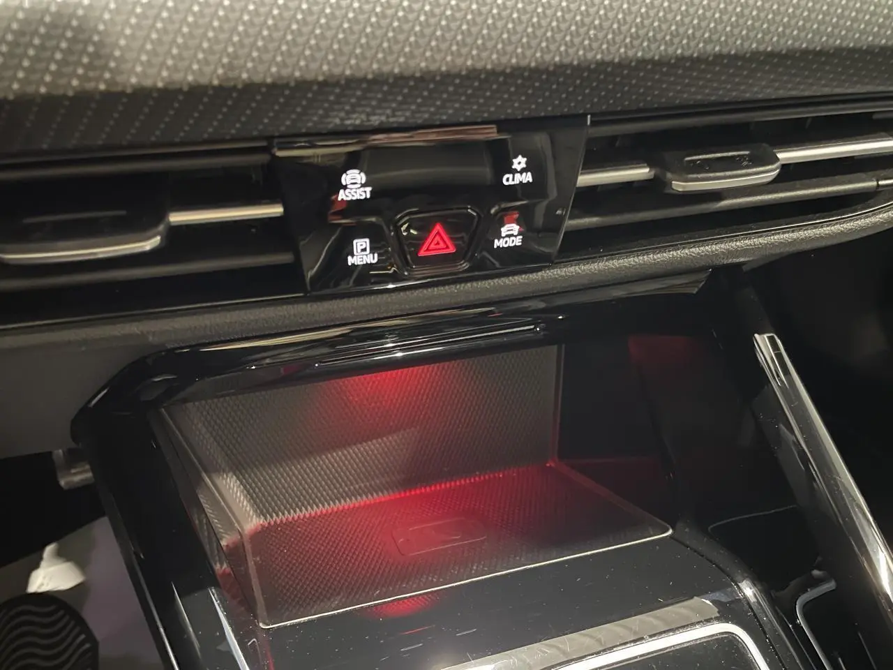 Gros plan sur la console centrale noire avec zone de charge à induction éclairée en rouge dans une Volkswagen Golf VIII R-Line blanche.