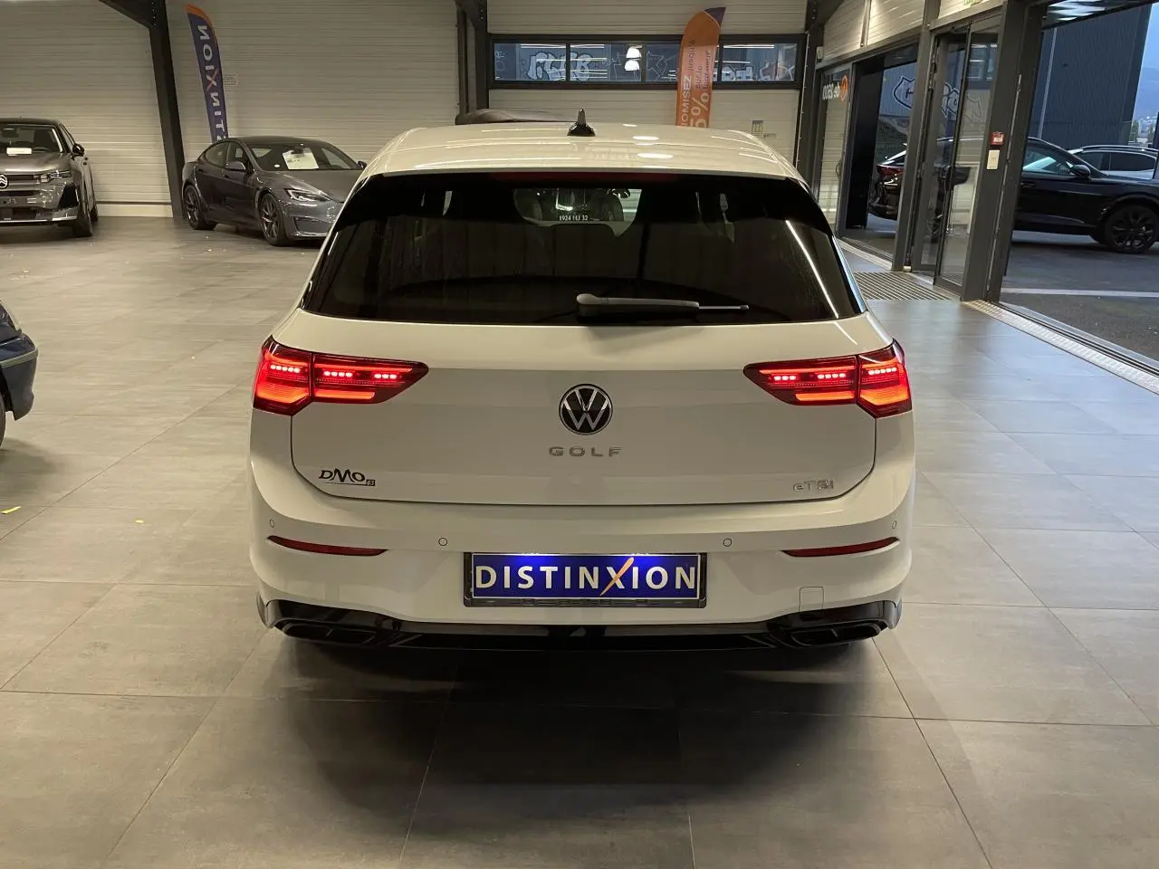 Vue arrière d'une Volkswagen Golf blanche 2024 avec feux LED allumés dans un showroom.