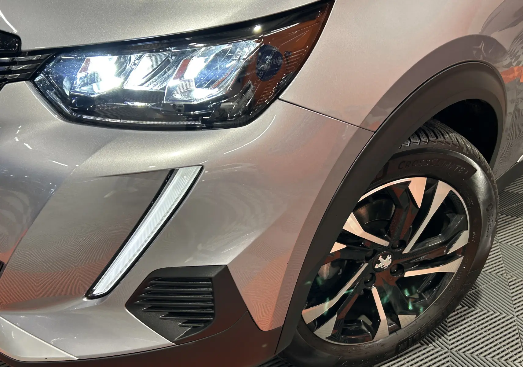 Gros plan sur l’avant droit gris Artense du Peugeot 2008 avec phare LED allumé et jante alliage bicolore.