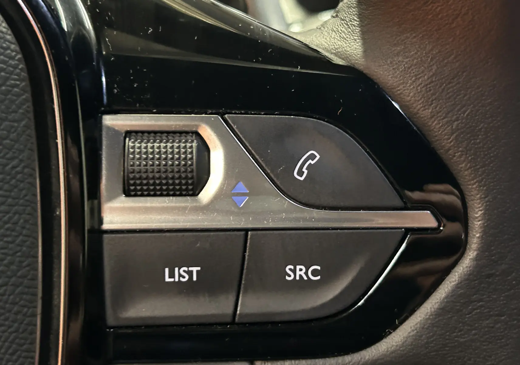Gros plan sur les commandes noires du volant côté gauche du Peugeot 2008 gris Artense, avec boutons LIST, SRC et téléphone.