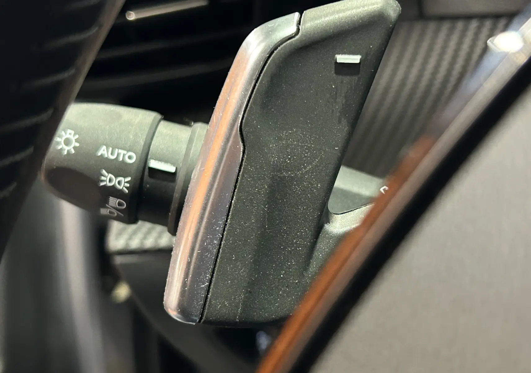 Gros plan sur la commande des phares avec fonction AUTO, située côté gauche du volant d’un Peugeot 2008 Gris Artense.
