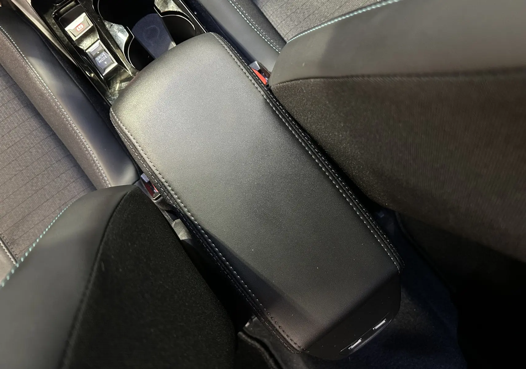 Vue rapprochée de l'accoudoir central noir entre les sièges avant du Peugeot 2008 gris Artense, intérieur tissu et cuir.