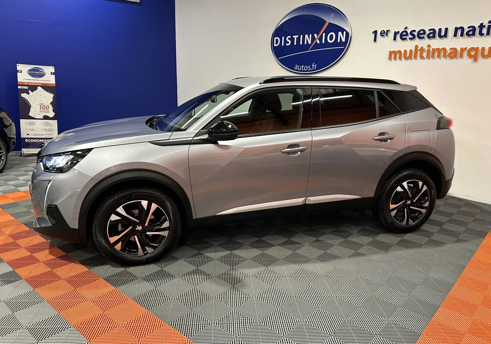 Profil côté gauche d’un Peugeot 2008 gris Artense 2023 en showroom avec jantes bi-ton et toit noir.