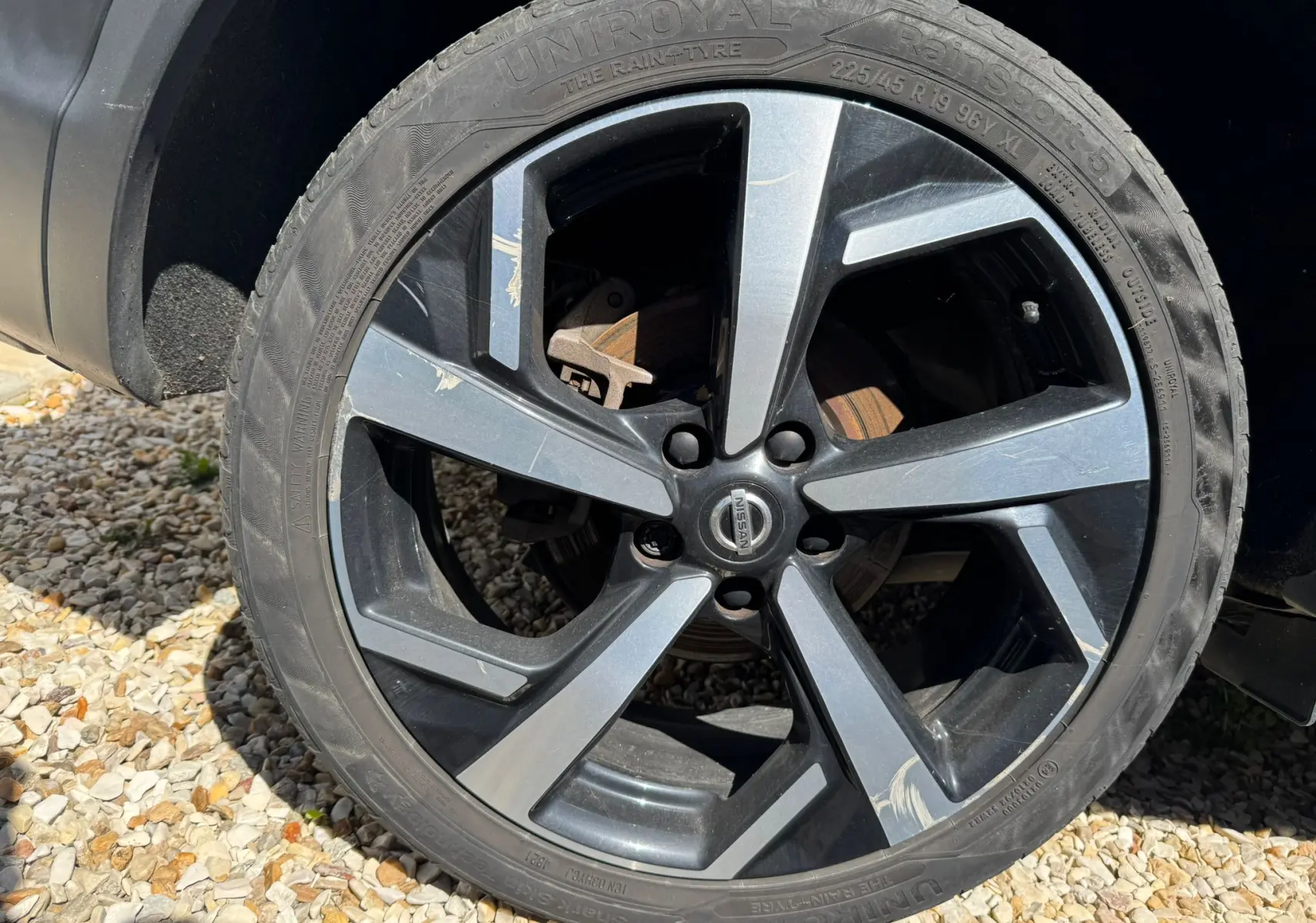 Gros plan sur la jante alu noire et grise du côté gauche d’un Nissan Qashqai noir, avec pneu Uniroyal visible.
