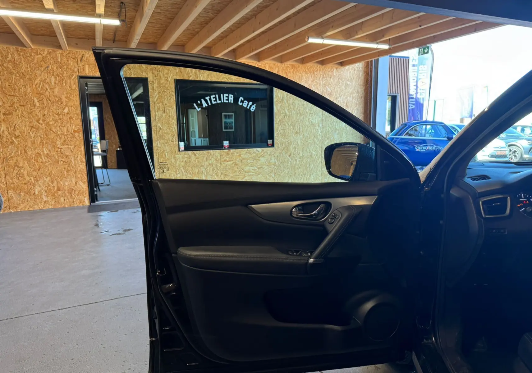 Vue intérieure côté gauche de la porte avant ouverte d'un Nissan Qashqai noir, montrant les commandes et poignée intégrées.