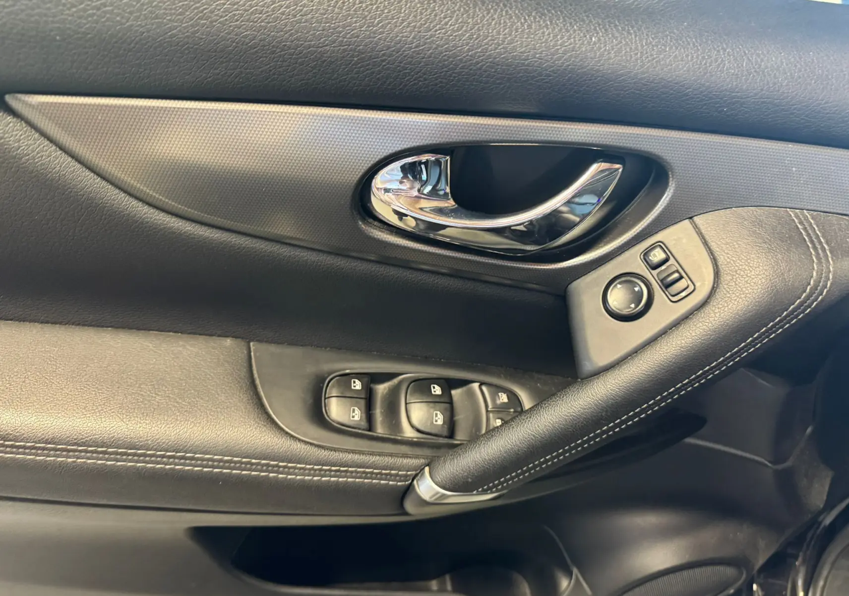 Gros plan sur la porte intérieure côté conducteur du Nissan Qashqai noir, avec poignée chrome et commandes électriques.